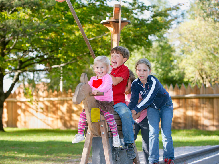 Drei Kinder spielen auf einem Holzpferd auf dem Happy Club Spielplatz
