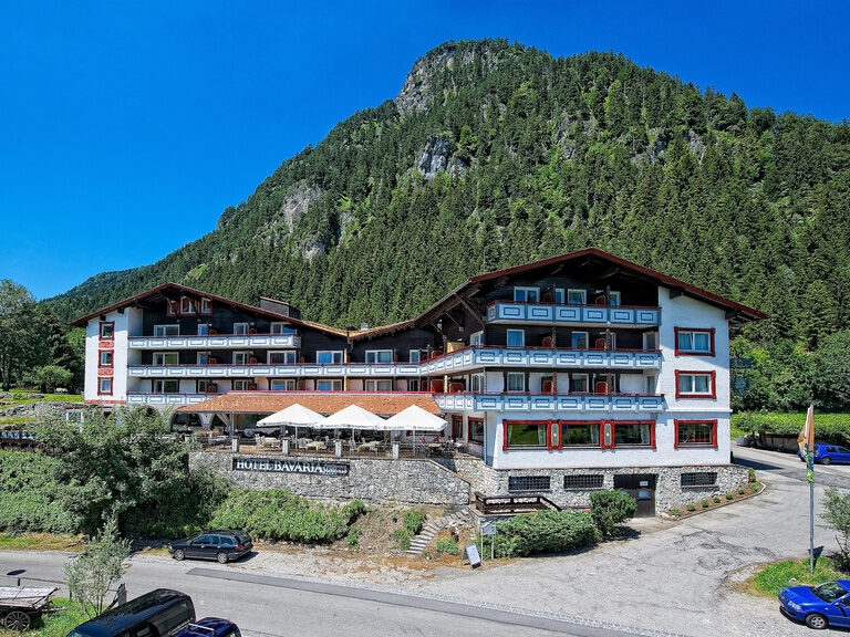Das weiß-rote Gebäude des Hotels Bavaria Pfronten in einer Alpenlandschaft.